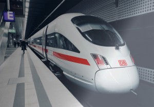 A Deutsche Bahn train stands on the track. A person in a dark coat is walking along the track