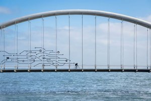 A cyclist rides across a modern arch bridge over the sea; behind him, digital circuit board overlays symbolize data migration and digital transformation