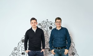 Zwei Männer vor neutraler Wand mit CPU strängen im Hintergrund