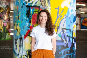 Celina Müller steht vor einer farbigen Graffiti-Wand