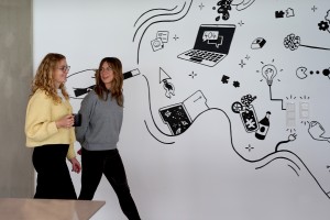 two women walking in front of a wall with illustrations