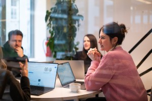 Eine Frau sitzt mit ihren Kolleg:innen am Tisch mit Laptops
