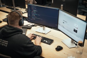 Ein Mann sitzt im Büro am Computer mit zwei Bildschirmen, auf denen Programmiercode zu sehen ist.