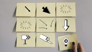 Hand nimmt ein Post It von 9, mit verschiedenen Ilustrationen drauf