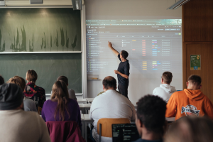 daniel weisser ist im hörsaal mit studierenden und hält eine präsentation.